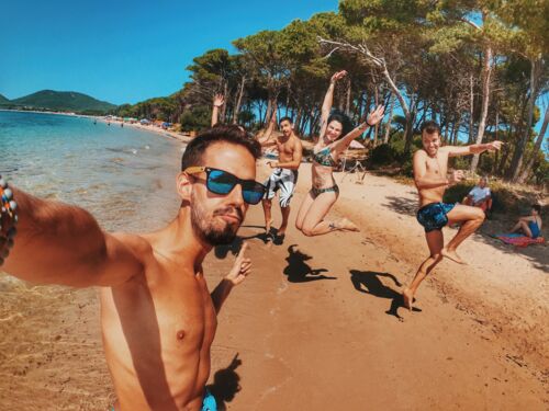 junge Leute springen ausgelassen am Strand herum und machen ein Selfi